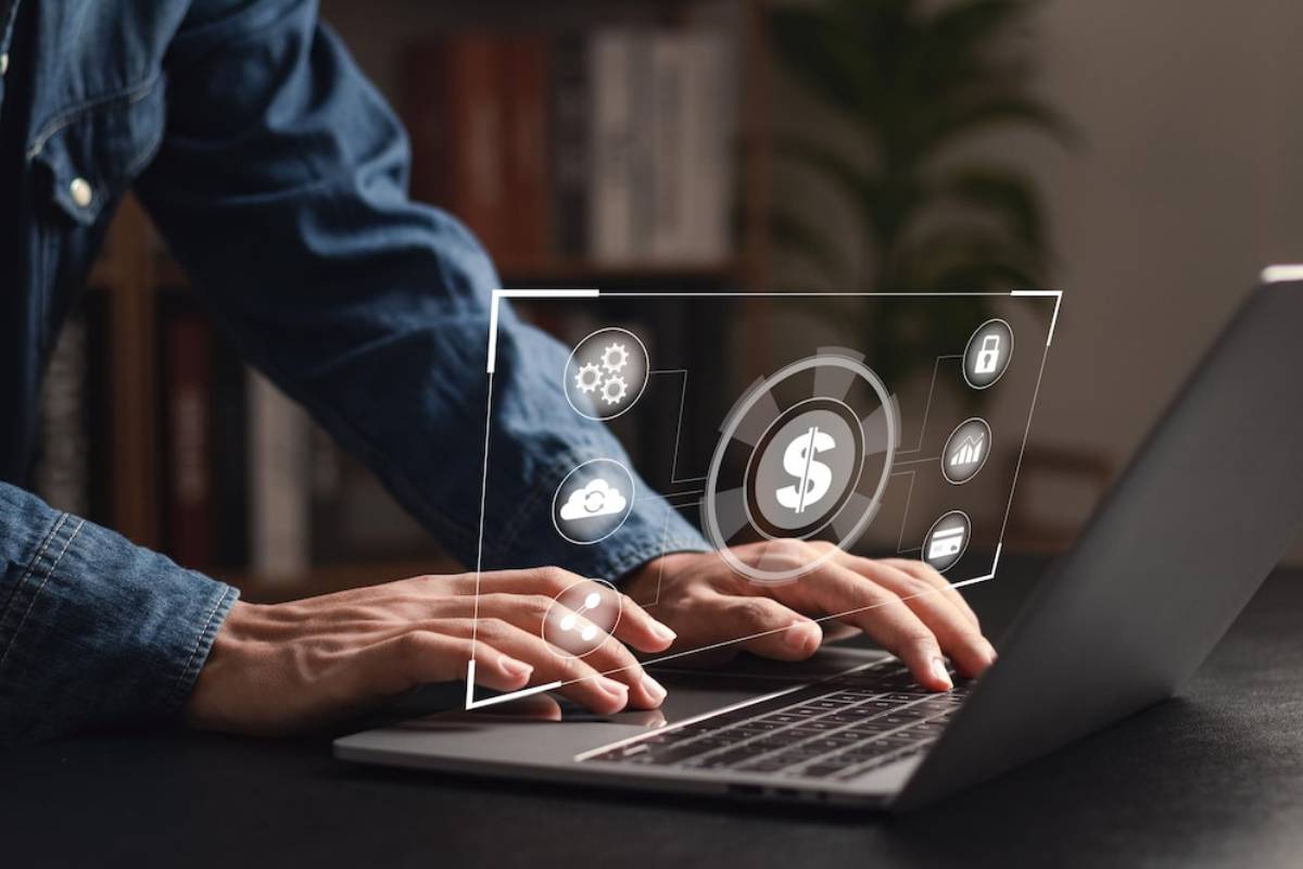 A person using a laptop with digital icons representing finance, security, and data management hovering above the keyboard.