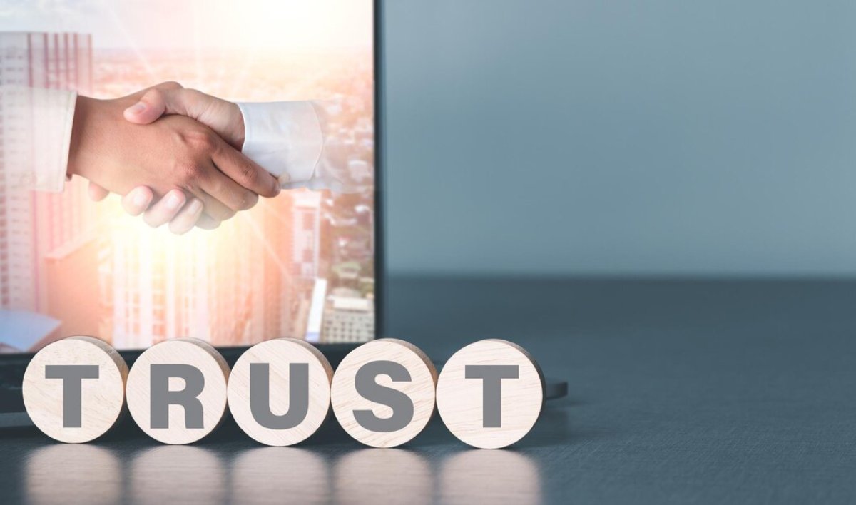 A close-up of a handshake with the word TRUST spelled out in wooden letters, symbolizing partnership and confidence in business.