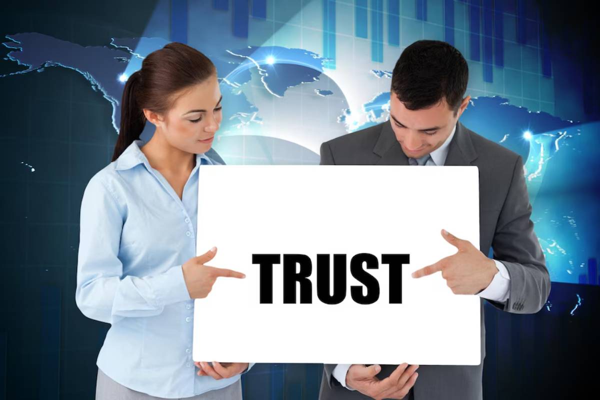 Two professionals stand together, holding a sign that boldly displays the word TRUST, against a backdrop of a digital world map.