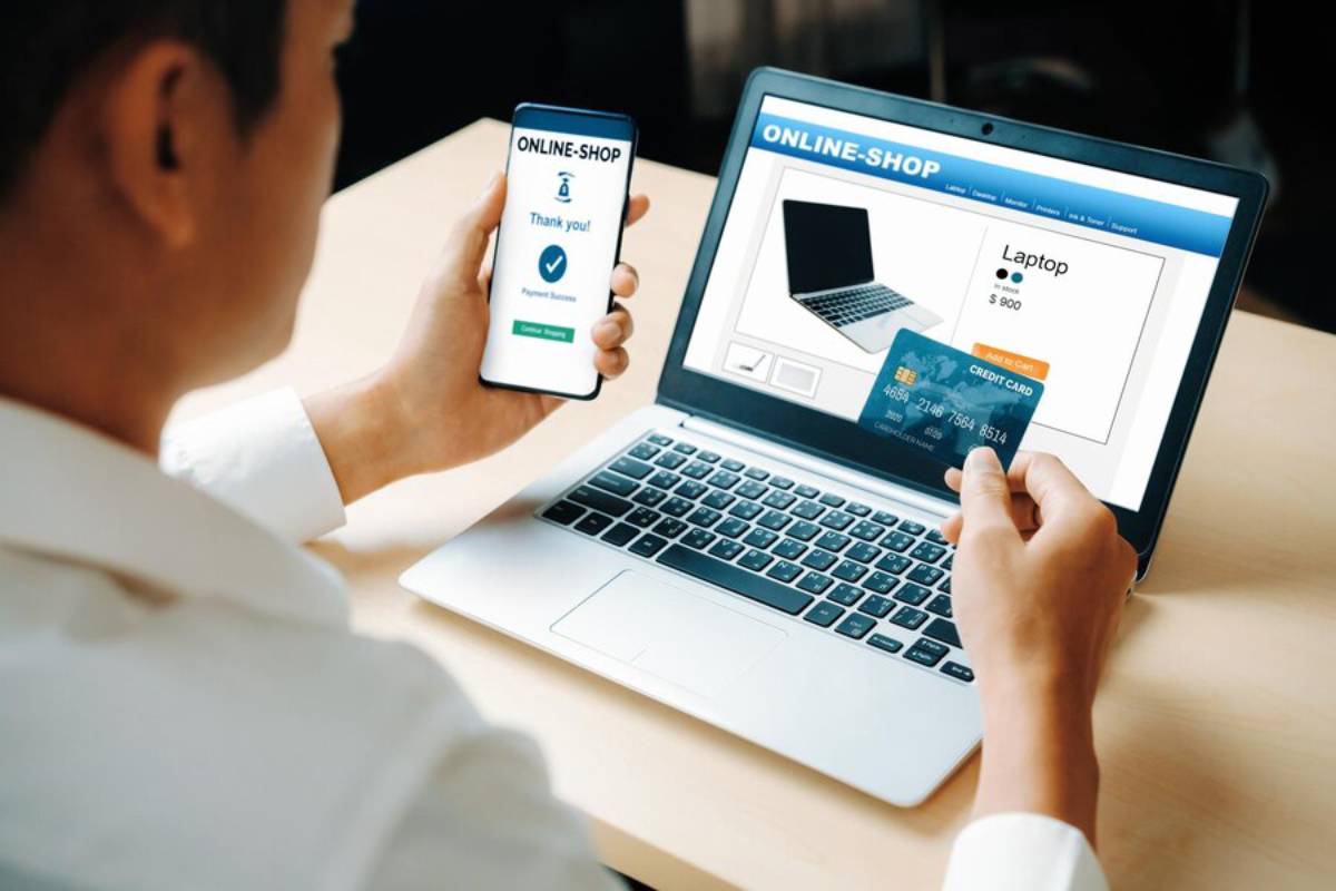 A person shops online, viewing a laptop priced at $900 on their laptop while confirming a successful payment on their smartphone.