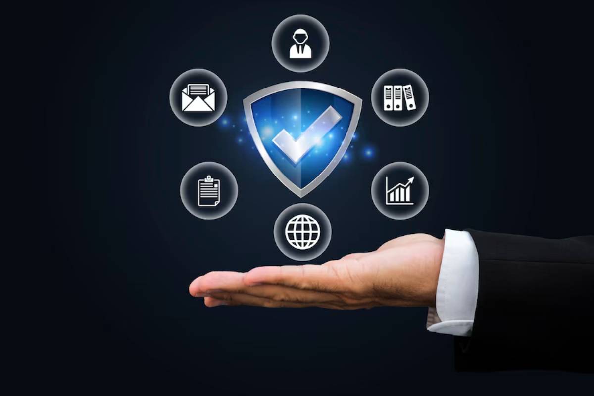 A business person's hand supports a digital shield symbol, surrounded by icons representing security, data, and communication.