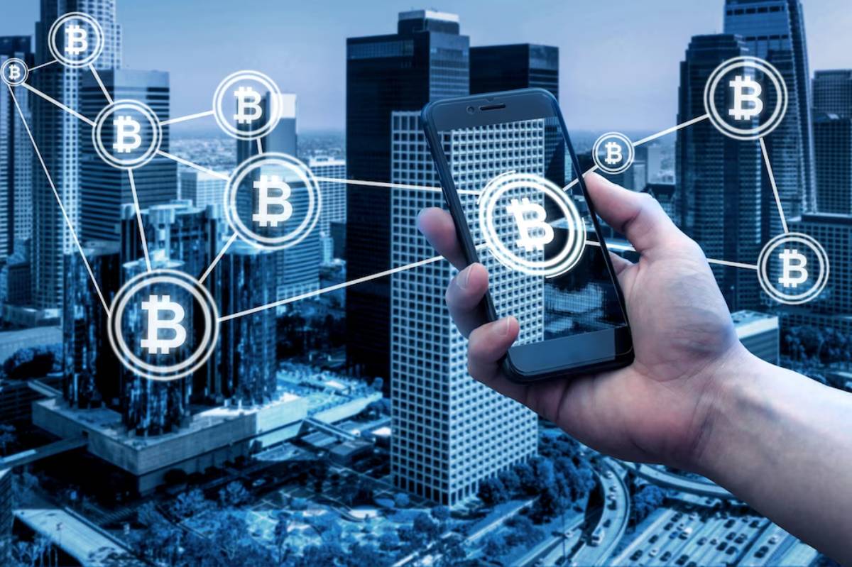A hand holding a smartphone displays Bitcoin symbols connected by lines, set against a city skyline in blue tones.
