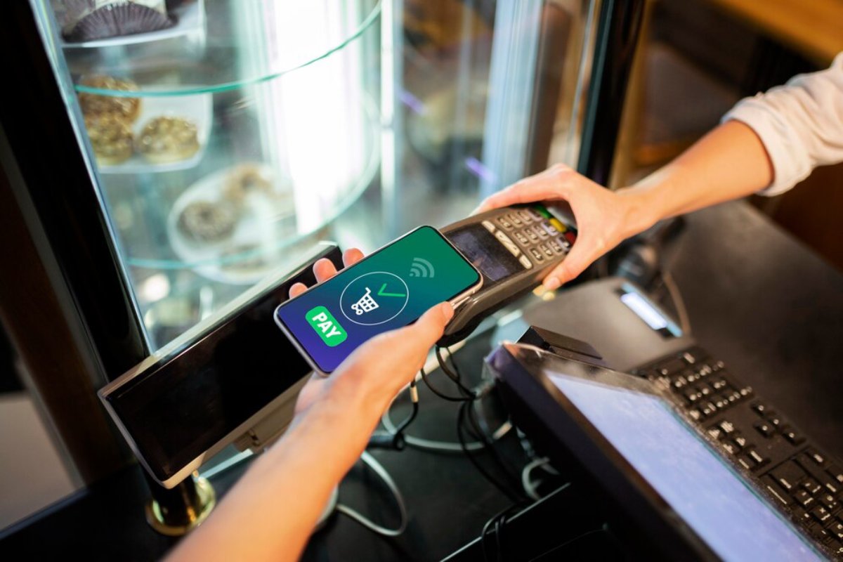 A person uses a smartphone to make a contactless payment at a point-of-sale terminal in a store.