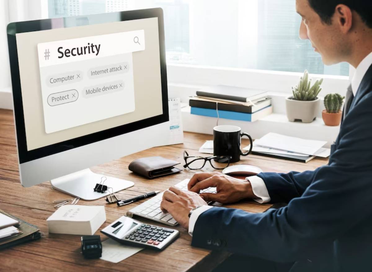 An office scene featuring a person typing on a computer displaying security topics related to technology protection.