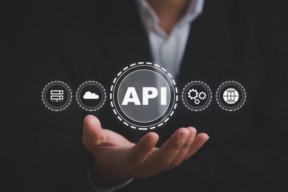 A person in a suit extends their hand, showcasing an API graphic surrounded by icons representing cloud, servers, gears, and a globe.