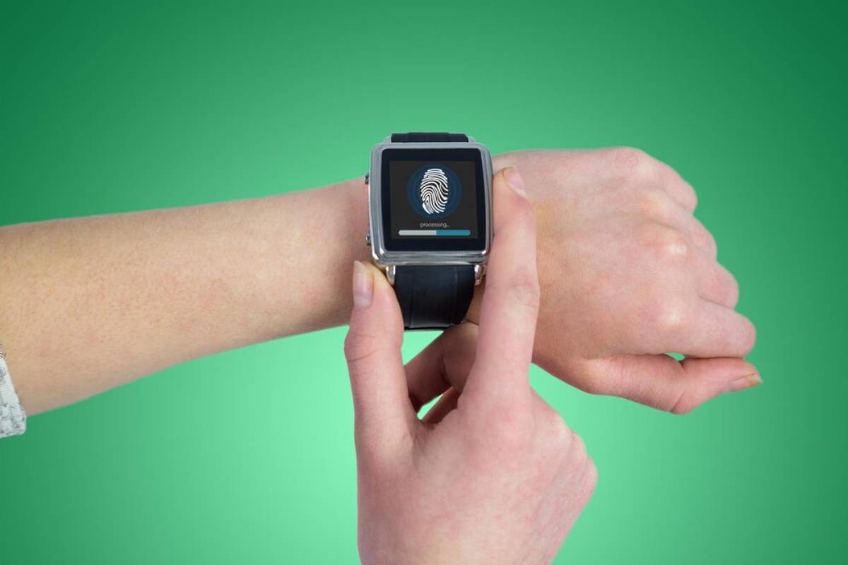 A hand is using a smartwatch displaying a fingerprint and processing message on a green background.