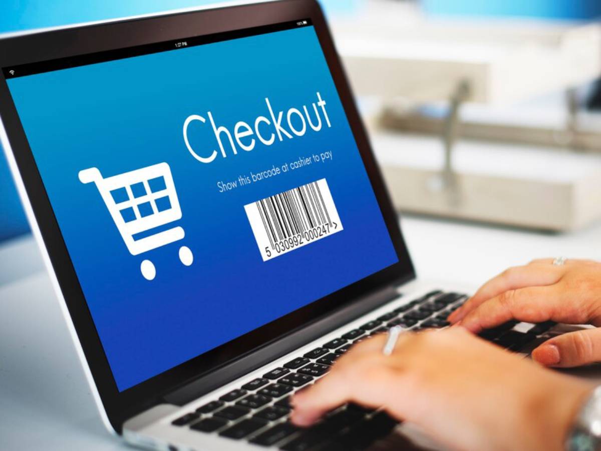 A laptop screen displays a checkout page with a shopping cart icon and a barcode, while a person's hand types on the keyboard.