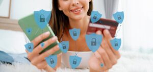 A person holds a smartphone and a credit card, surrounded by digital icons of shields symbolizing online security and privacy.