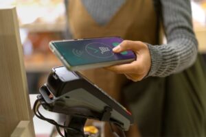 A person using a smartphone for contactless payment at a checkout terminal, highlighting modern payment technology.