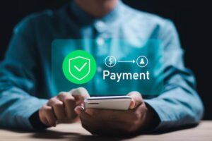 A person in a blue shirt uses a smartphone, with a green payment icon and check mark overlay, symbolizing secure online transactions.
