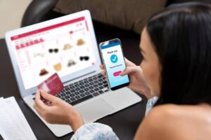 A person holds a credit card and smartphone displaying a payment confirmation while shopping online on a laptop.