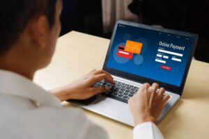 A person is making an online payment on a laptop, with a credit card interface displayed on the screen.
