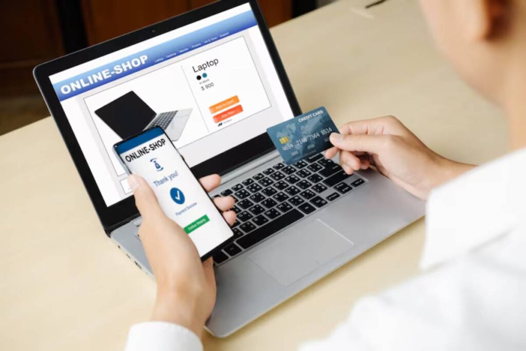 A person holding a smartphone displaying a payment confirmation, while ready to purchase a laptop online with a credit card.